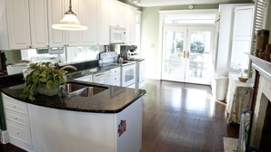 A kitchen with white cabinets, a black countertop, and a central island with a sink. - Desoto Beach Bed & Breakfast (Tybee Island)