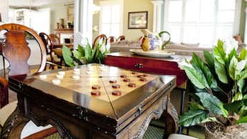 A checkered game board on a wooden table in a room with a dining area, a sofa, and potted plants.