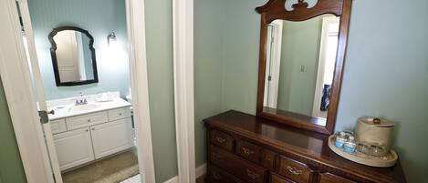 A bathroom with a white vanity, a large mirror, and a wooden dresser with drawers.