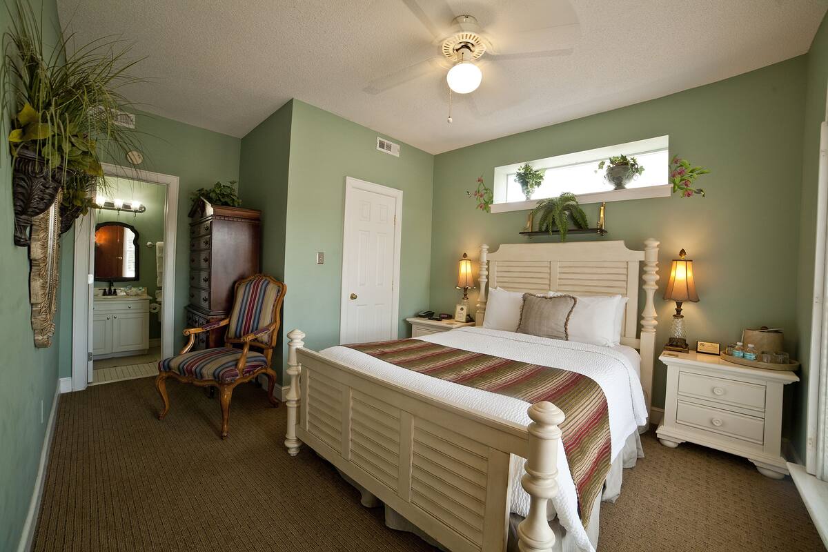 A bedroom with a large bed, two bedside tables with lamps, a chair, a dresser, and a mirror above the bed.