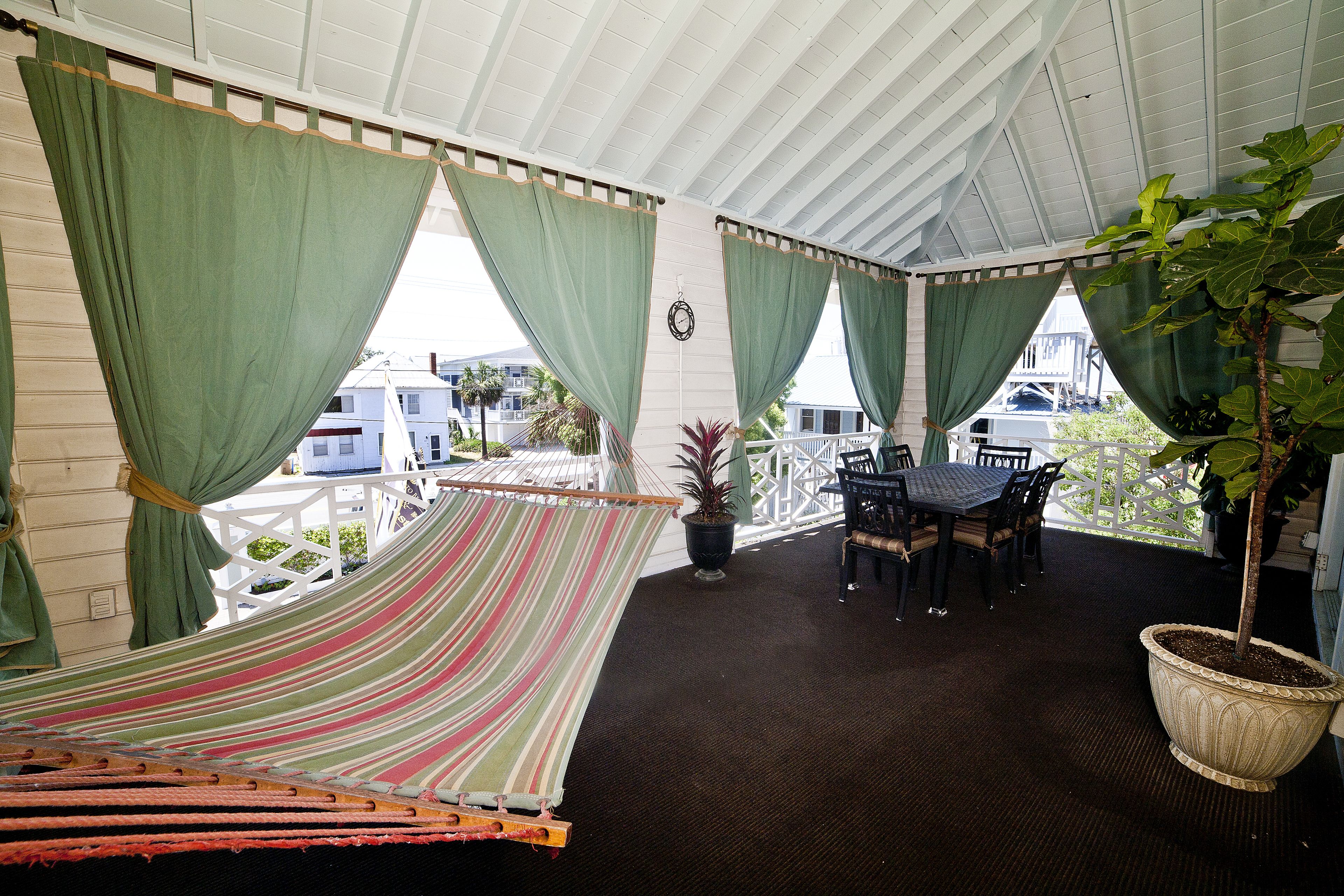 A covered outdoor seating area with a hammock, a table with chairs, and a potted plant.