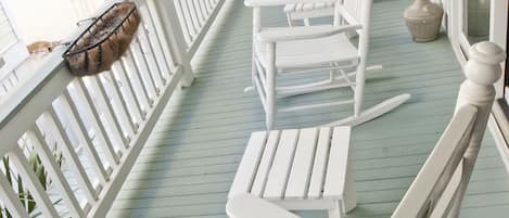 A porch with white rocking chairs and a white railing.