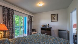 Une chambre d’hôtel comprenant un lit, un bureau avec un micro-ondes, un réfrigérateur, une chaise et un balcon avec des rideaux.