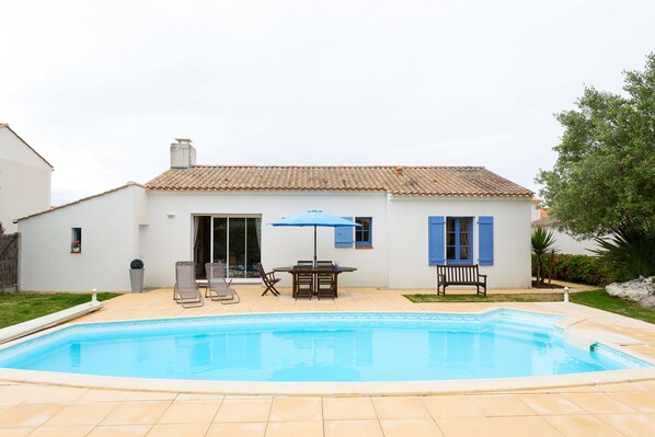 Una casa con piscina, un patio con mesa y sillas, y una sombrilla azul.