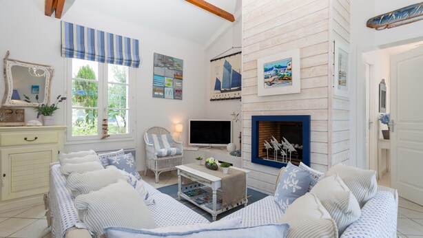 A living room with a sofa, a television, a fireplace, and a window with a view of greenery. - Madame Vacances Le Domaine de Vertmarines (Saint-Jean-de-Monts)