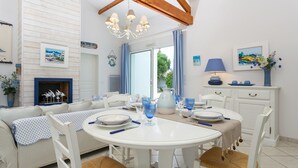 A dining area with a round table, white chairs, and blue glassware. There is a sofa with a patterned cover and a fireplace with decorative items. - Madame Vacances Le Domaine de Vertmarines (Saint-Jean-de-Monts)