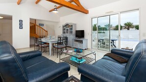 A living room with a sofa, a TV, and a dining area with chairs and a table. - Madame Vacances Le Domaine de Vertmarines (Saint-Jean-de-Monts)