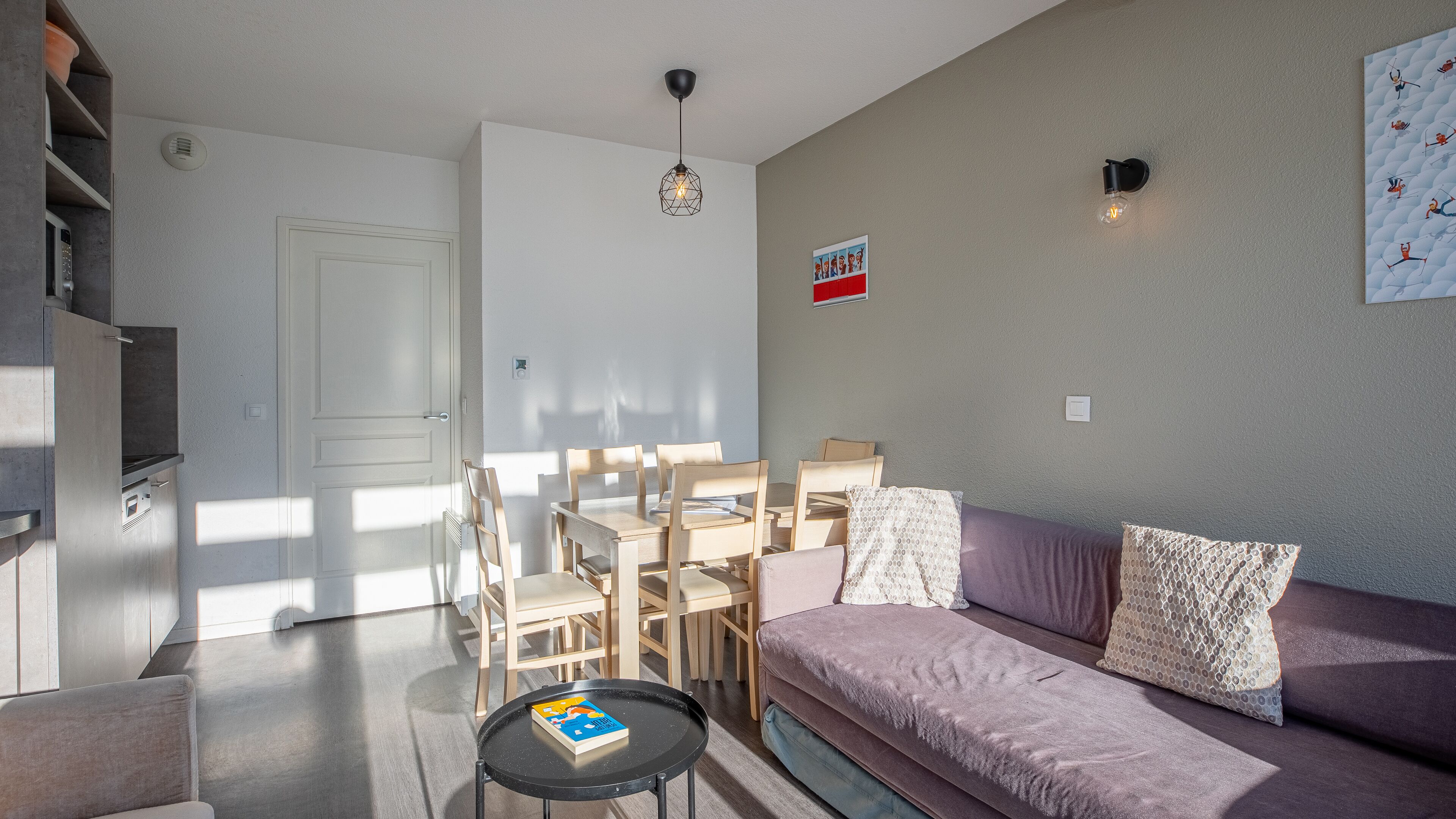 Een moderne woonkamer met een bank, een eettafel met stoelen, een bijzettafeltje met een boek en een hanglamp.