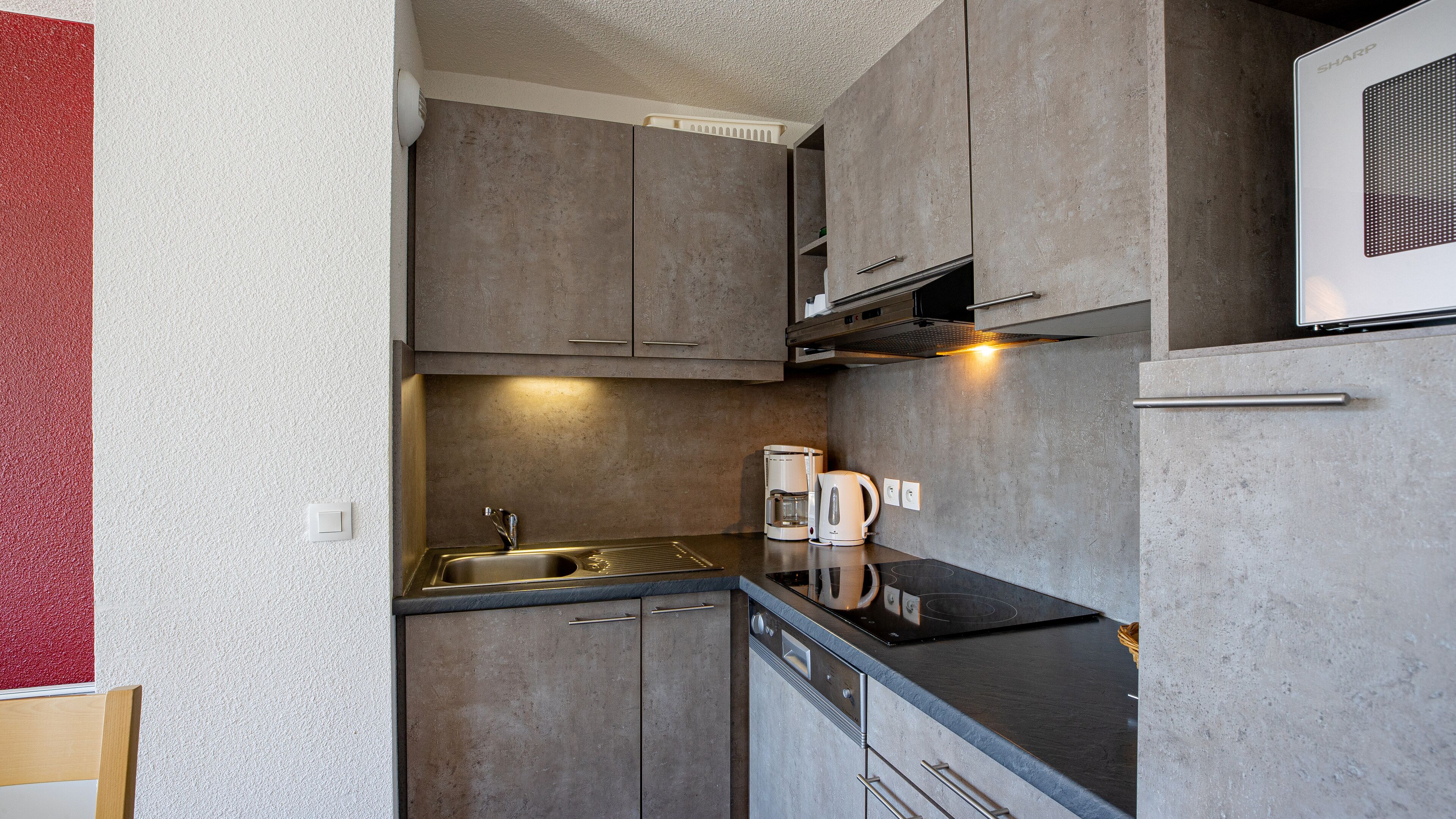 A compact kitchen with a sink, two coffee makers, and a built-in oven.
