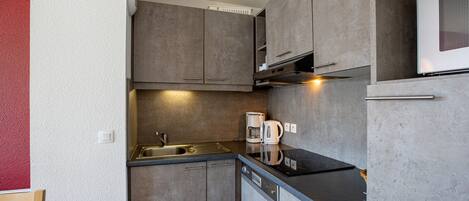 A compact kitchen with a sink, two coffee makers, and a built-in oven.
