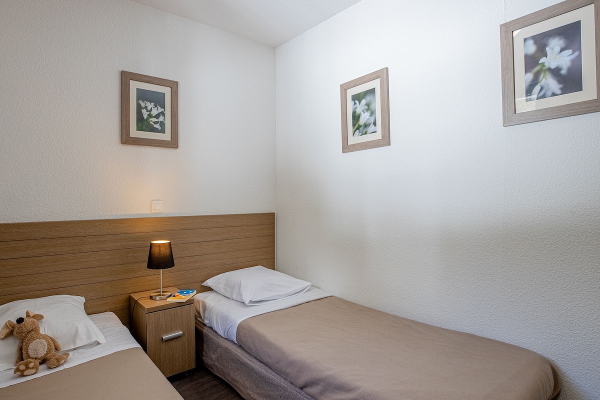 A hotel room with two beds, a wooden headboard, a nightstand with a lamp, and two framed pictures on the walls.