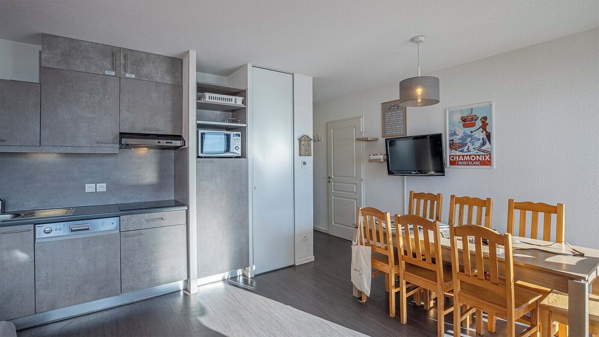 A modern kitchen with grey cabinets, a built-in oven, and a dining area with wooden chairs and a table.