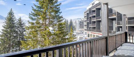 A balcony with a view of snow-covered trees and a building with a restaurant named "Restaurant Le Refuge".