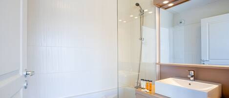 A modern bathroom with a glass-enclosed shower, a white bathtub, and a vanity with a sink and mirror.