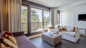 Ein modernes Hotelzimmer mit einer großen Schiebeglasdoor zum Balkon, einer Couch, einem Couchtisch und einem flachbildfernseher an der Wand.
