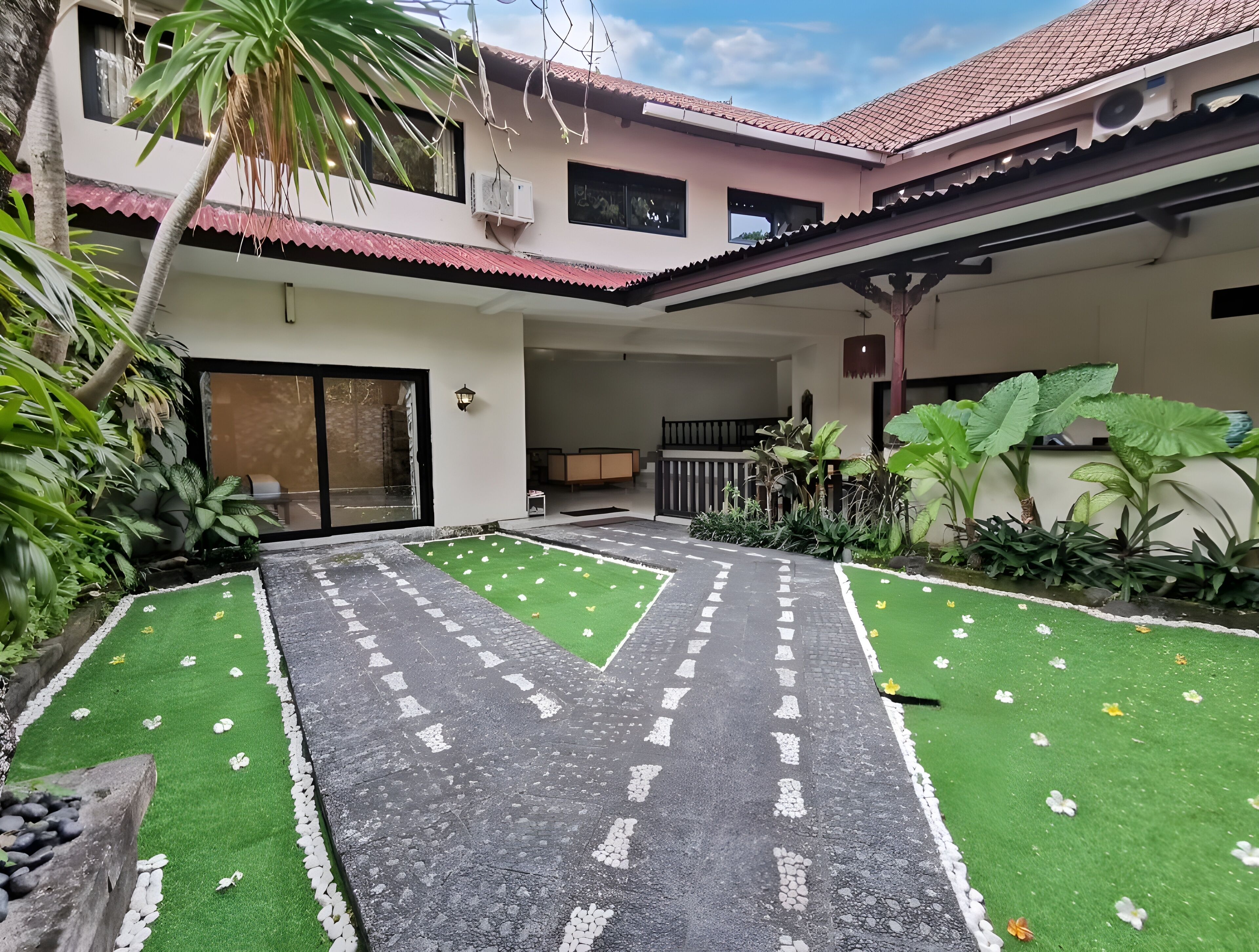 Une cour avec un chemin pavé, de l’herbe artificielle verte et diverses plantes.