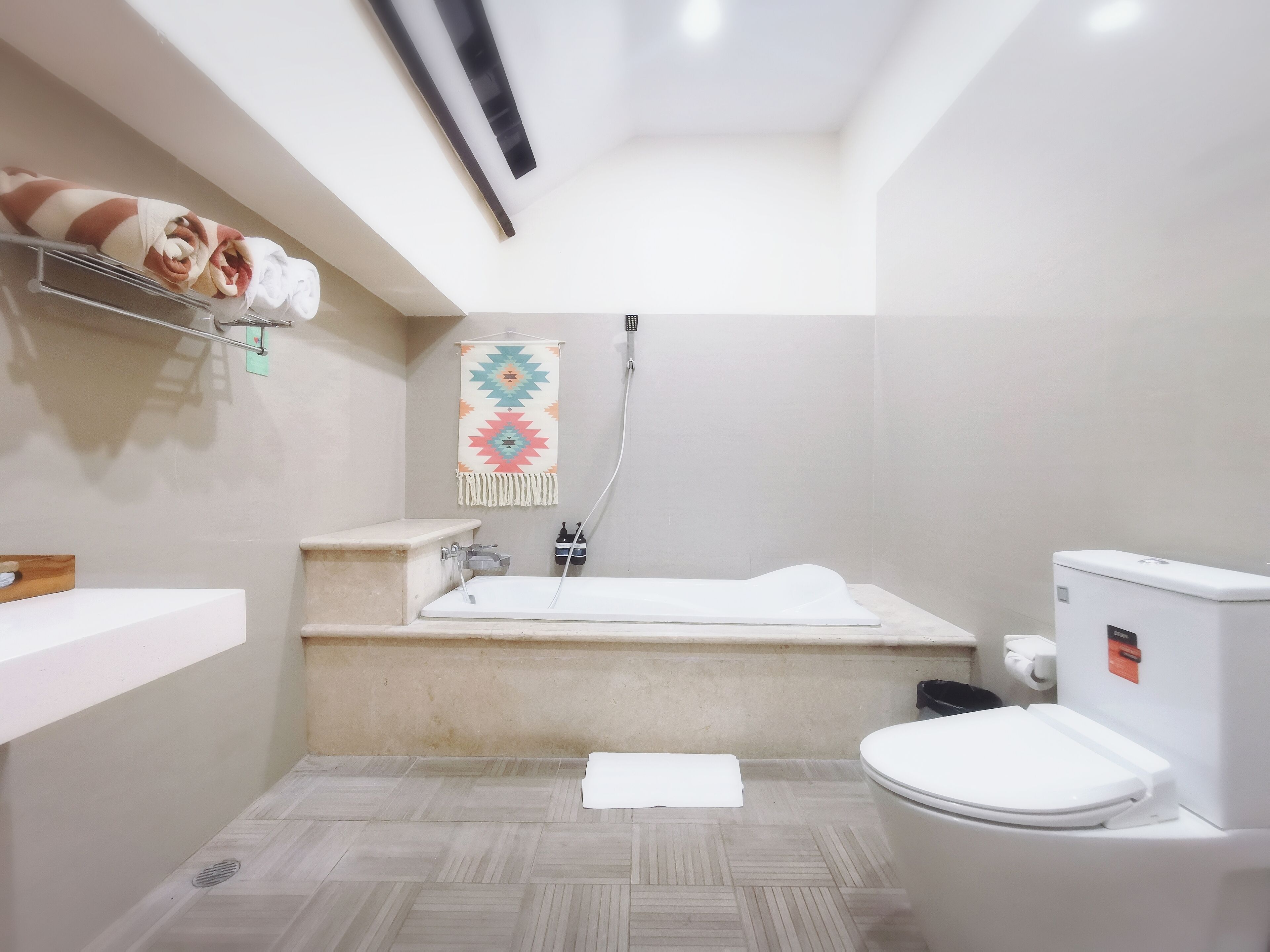 A small bathroom with a white toilet, a bathtub, and a shower. There is a towel on the floor and a shelf with towels above the bathtub.