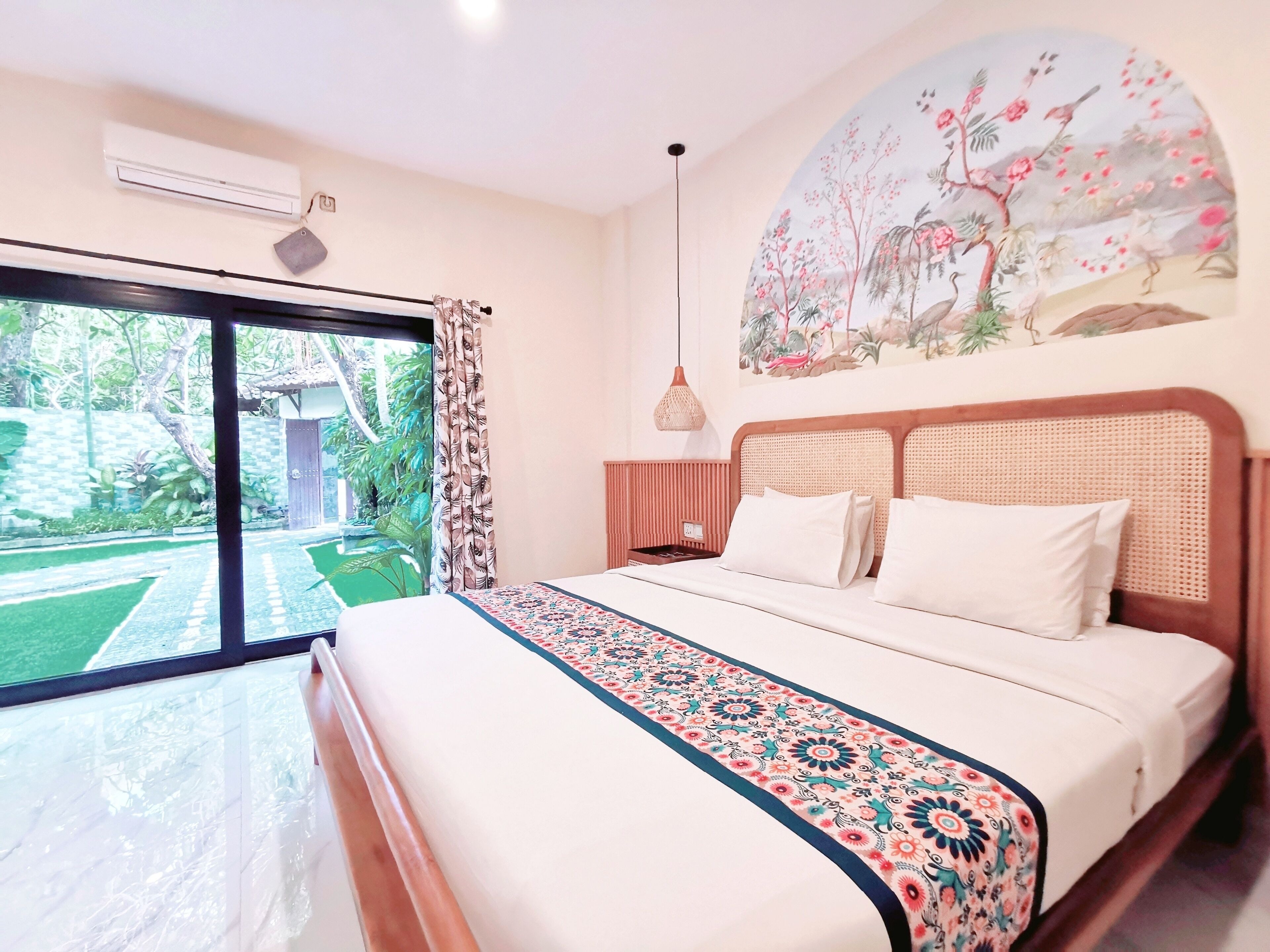 A bedroom with a large bed, a window with curtains, a wall-mounted air conditioner, and a painting.