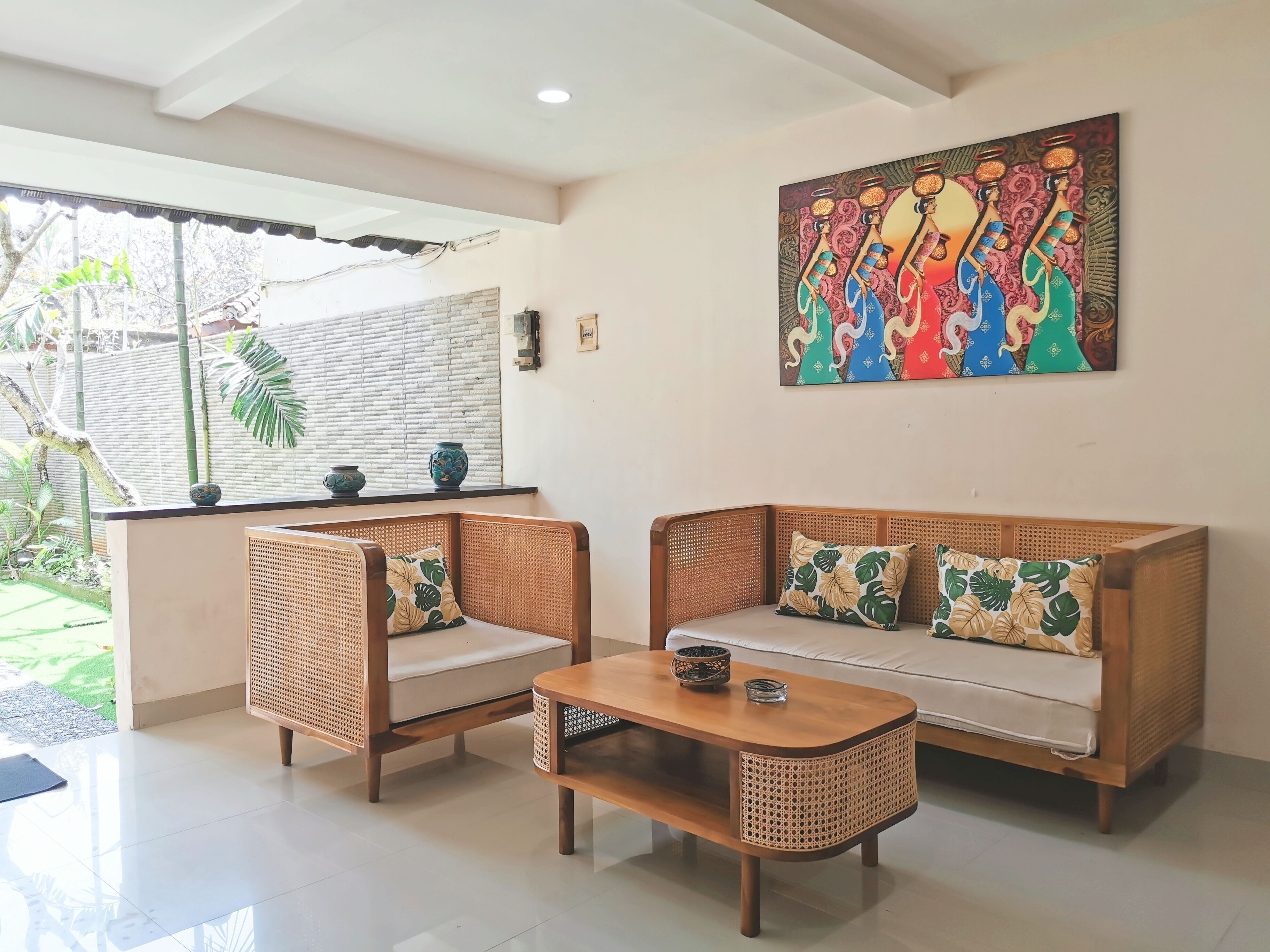 A room with two wicker sofas, a wooden coffee table, and a large painting on the wall.