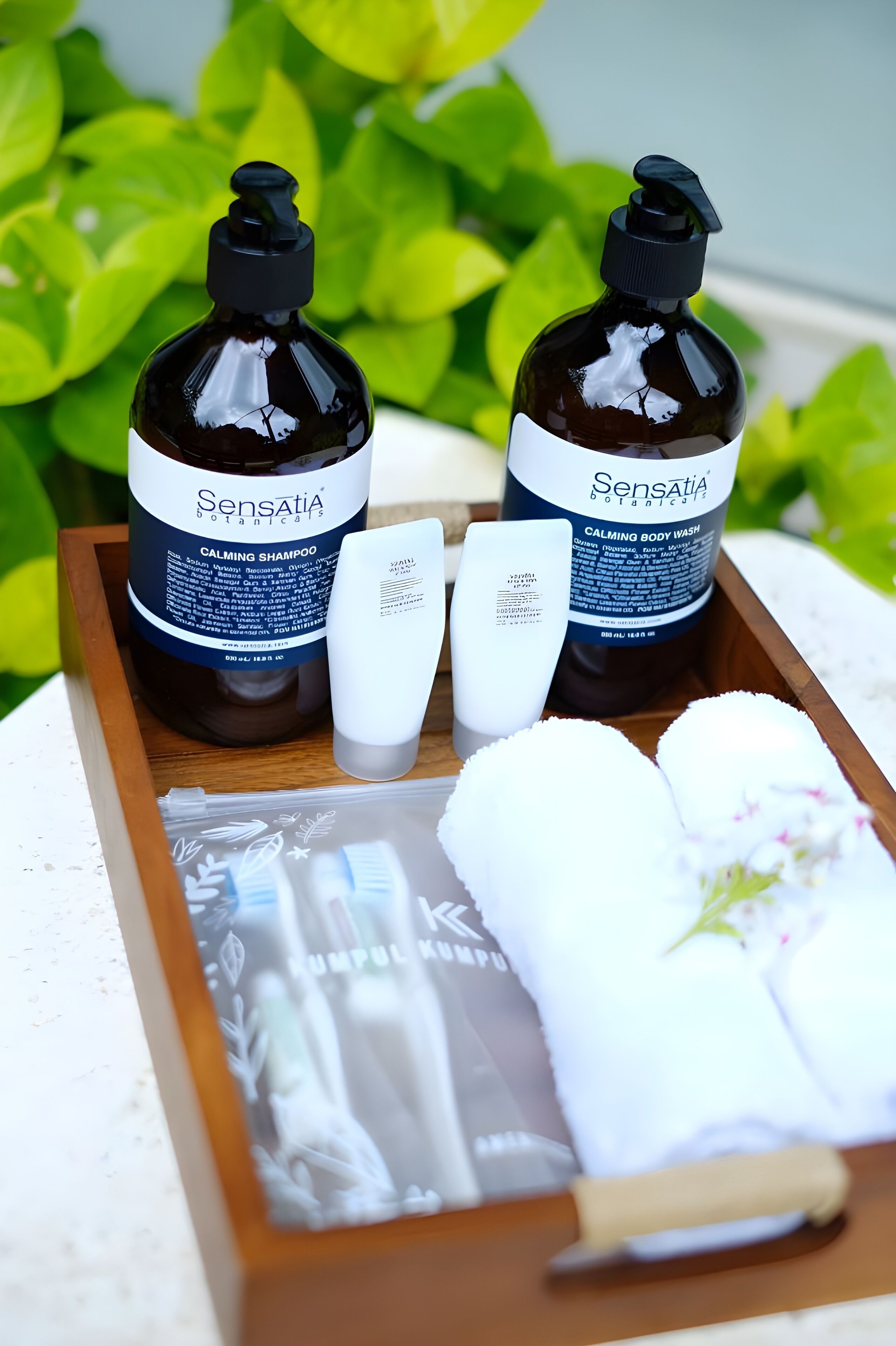 Ein hölzernes Tablett mit einer Sensatia Botanica beruhigenden Duschlotion, einer weißen Flasche und einem weißen Handtuch mit Blumenmuster.