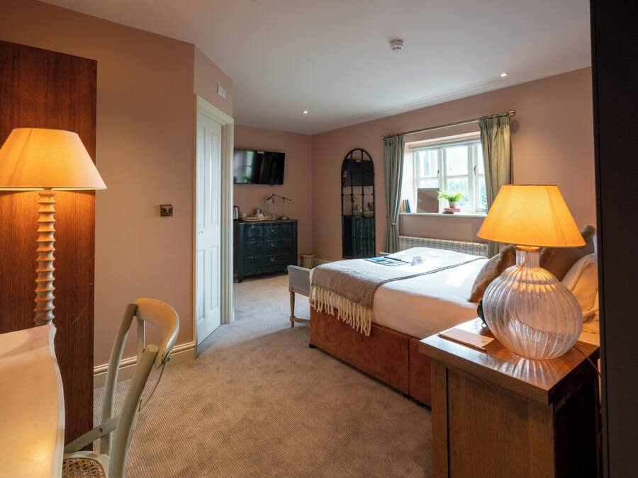 A bedroom with a bed, bedside lamps, a dresser, a television, and a window with curtains.