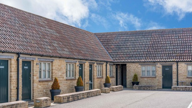 A building with a stone facade, multiple doors, and a gravel courtyard. - Crown Inn (Chippenham)