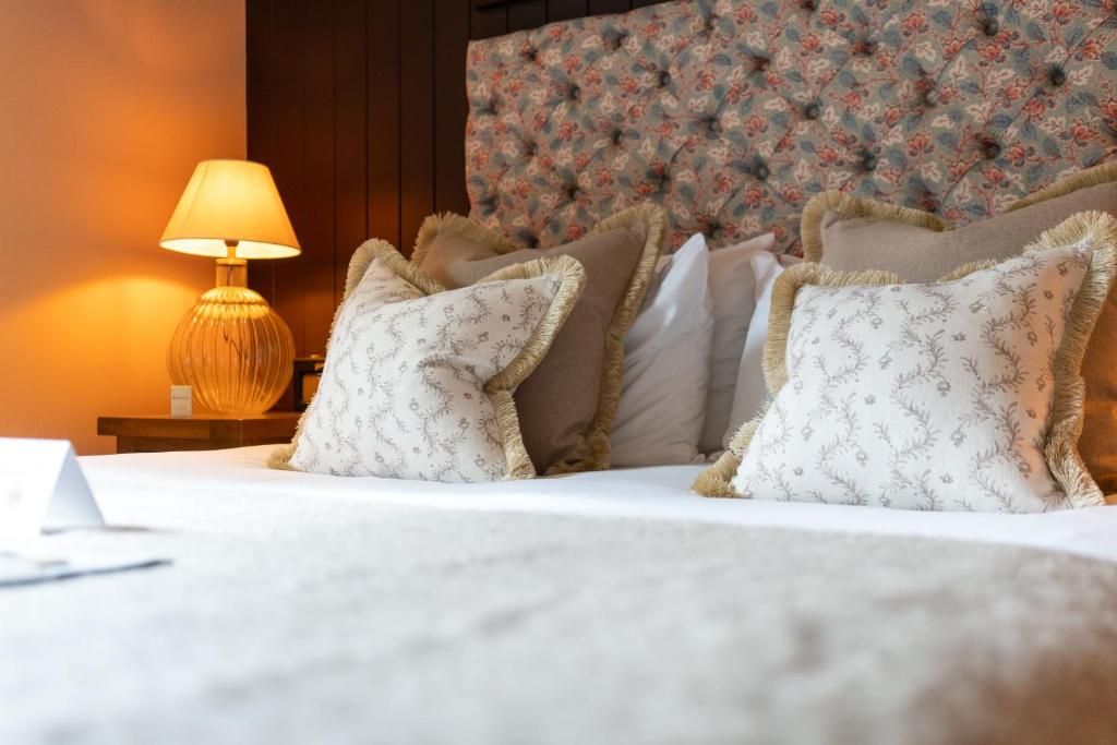 Un lit bien fait, agrémenté d’oreillers à motifs, d’une lampe de chevet et d’une tête de lit ornée de motifs floraux.