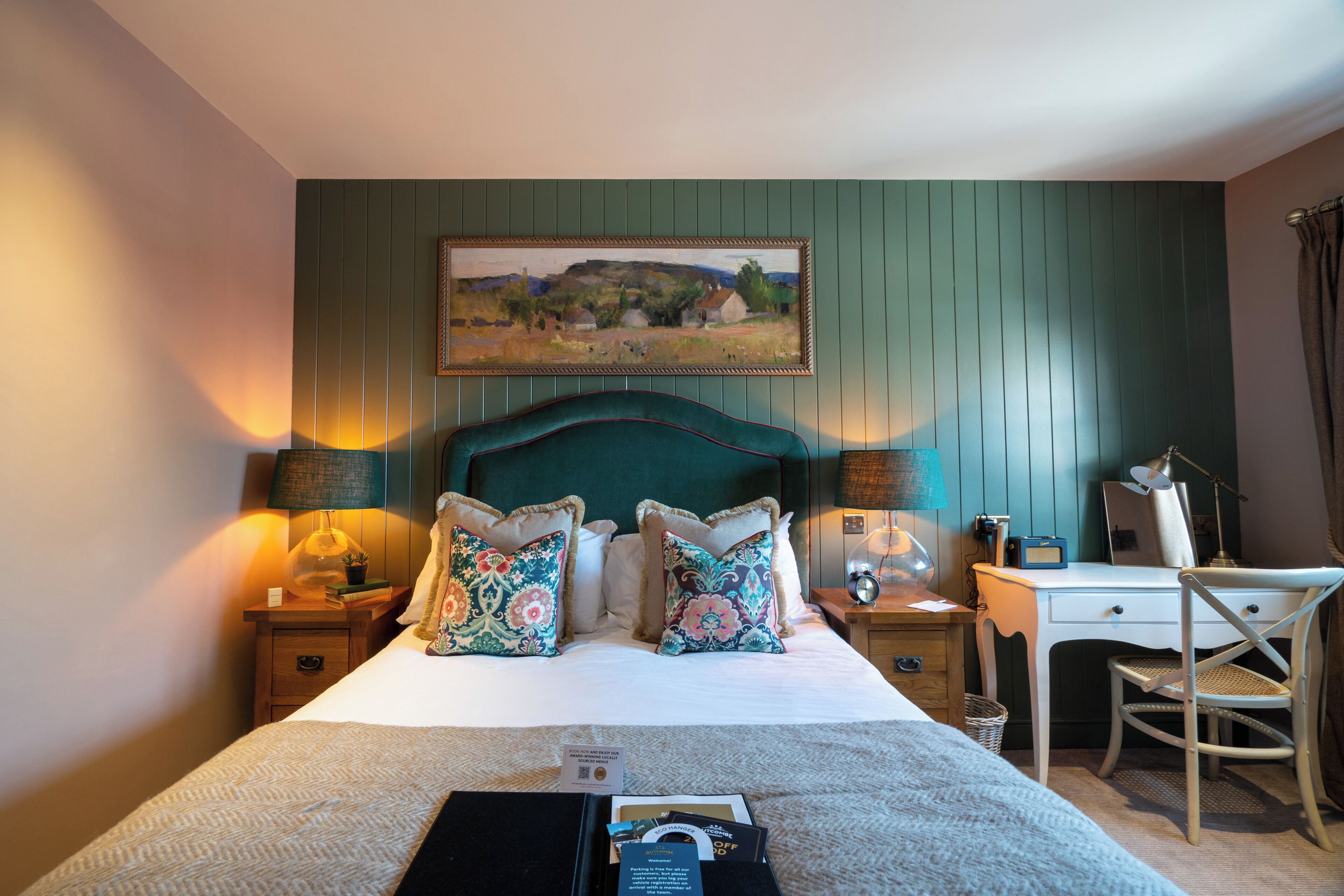 Een hotelkamer met een bed, twee nachtkastjes, een bureau, een stoel en een schilderij aan de muur.