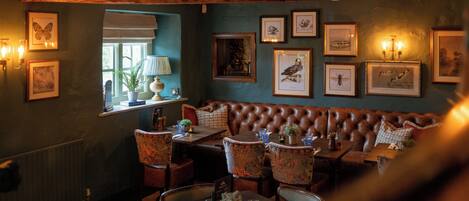 A cozy restaurant interior with a leather booth seating area, framed artwork on the walls, and a window with a view.