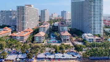 Um hotel moderno e alto, com vários andares, piscina e área de praia com guarda-sóis e espreguiçadeiras.