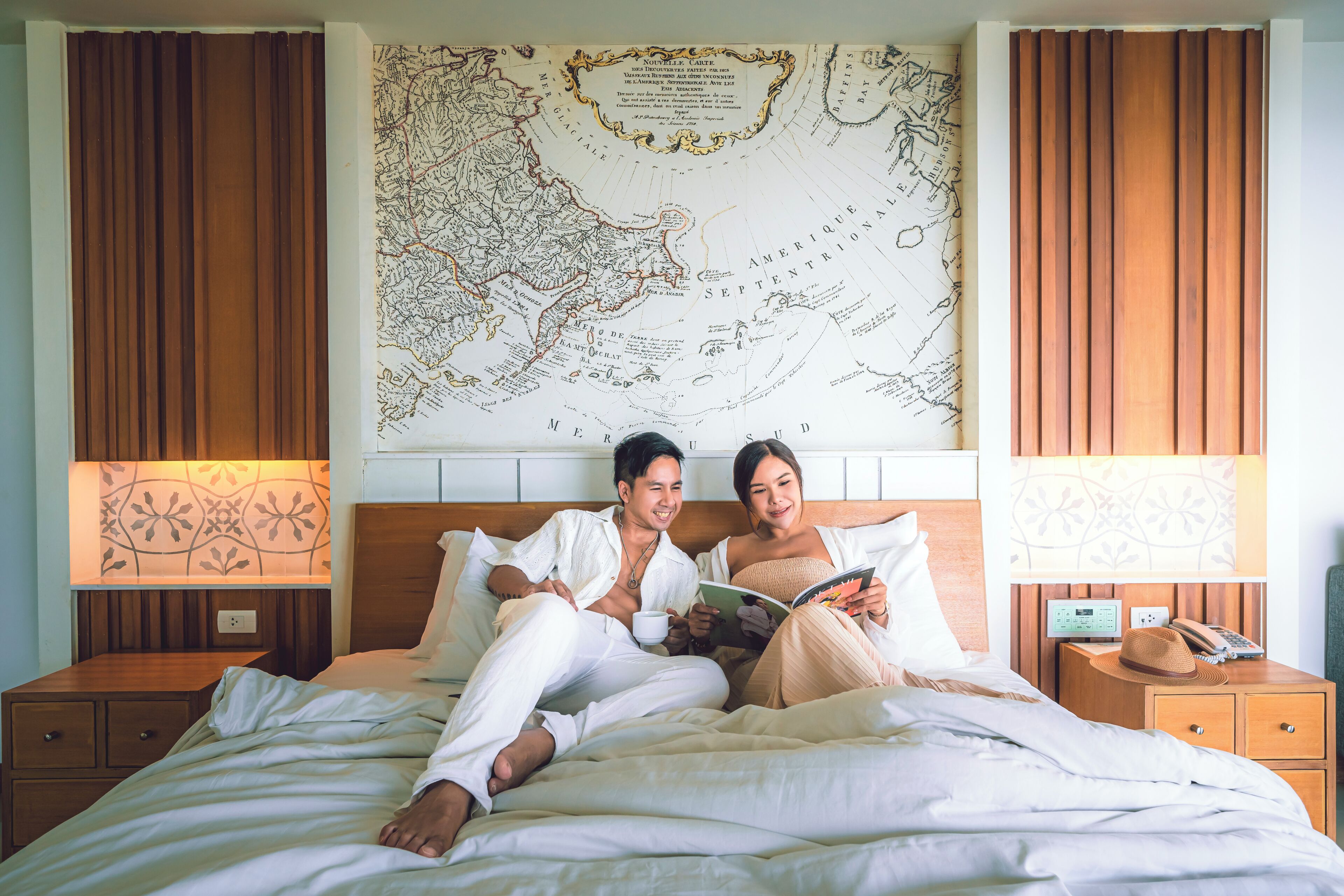 A bed with a map, two people reading, and a nightstand with a hat.