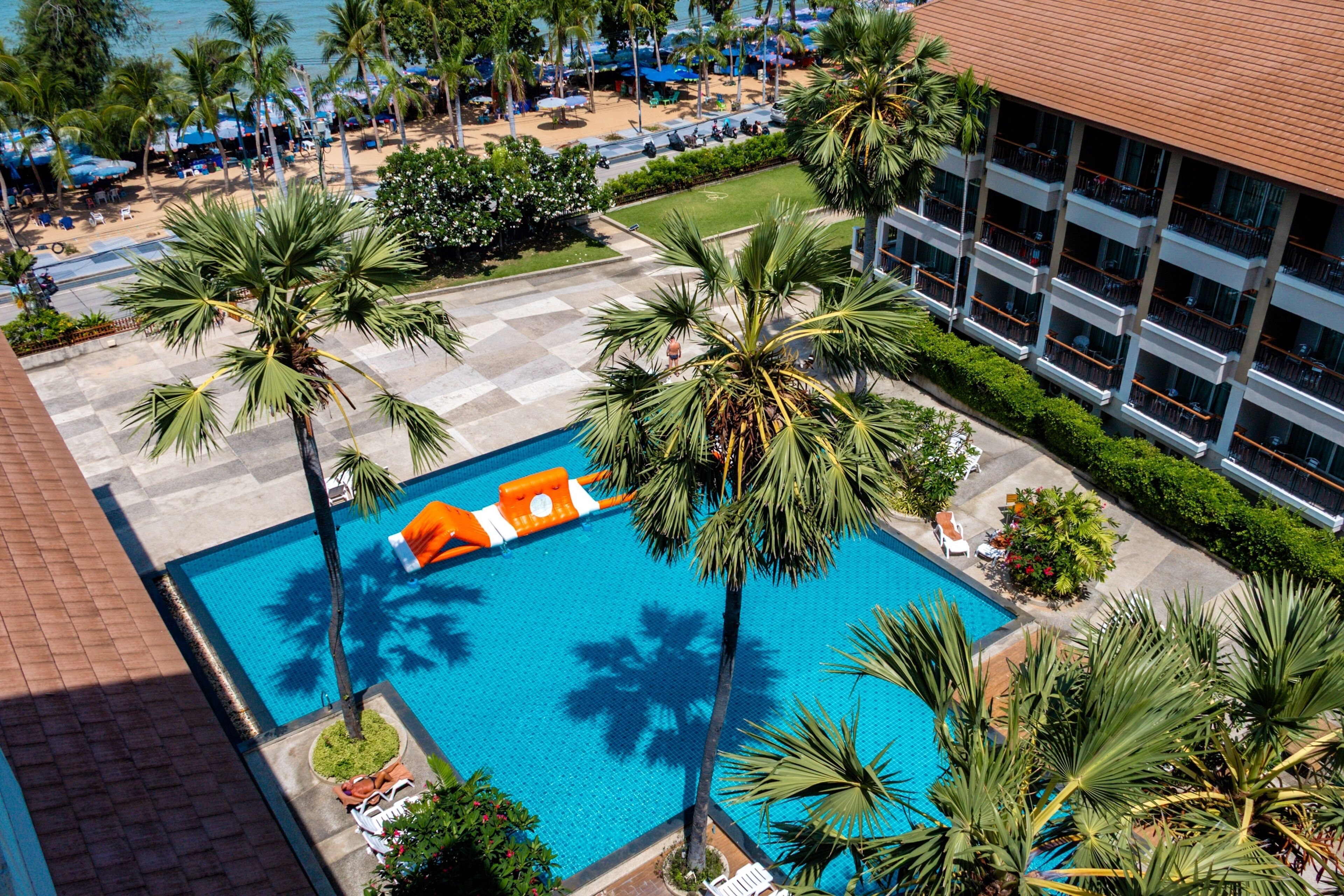 A hotel pool area with palm trees, lounge chairs, and a building with balconies.