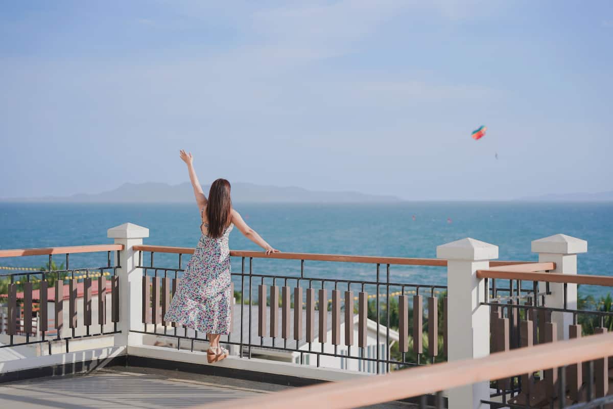A woman standing on a balcony with a view of the sea.