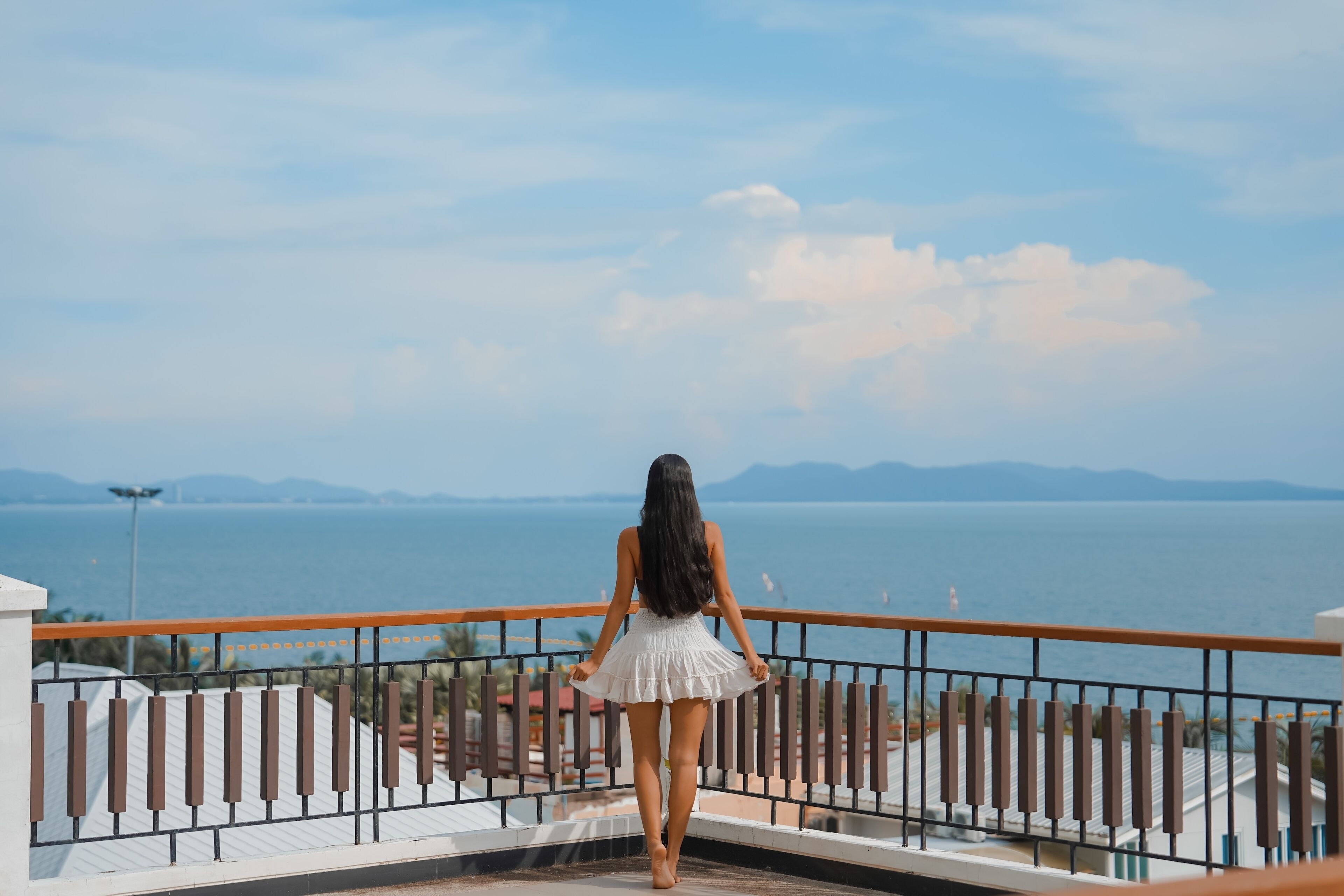 Eine Person steht auf einem Balkon mit Blick auf das Meer und entfernte Berge.