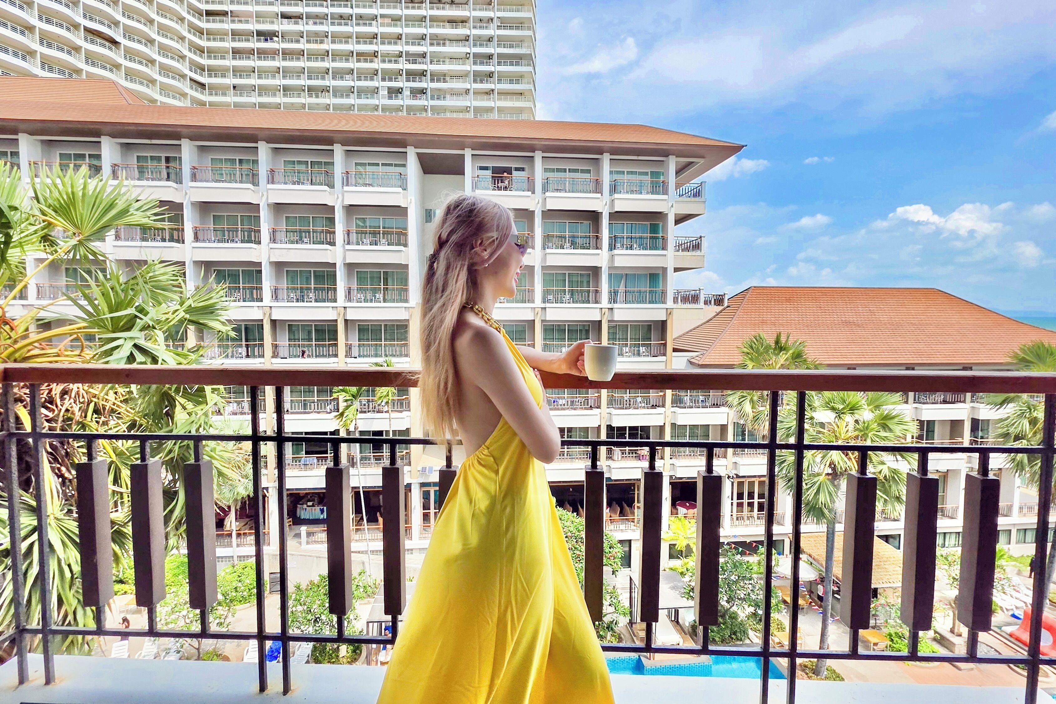 A high-rise hotel with multiple balconies, a swimming pool, and lush greenery.