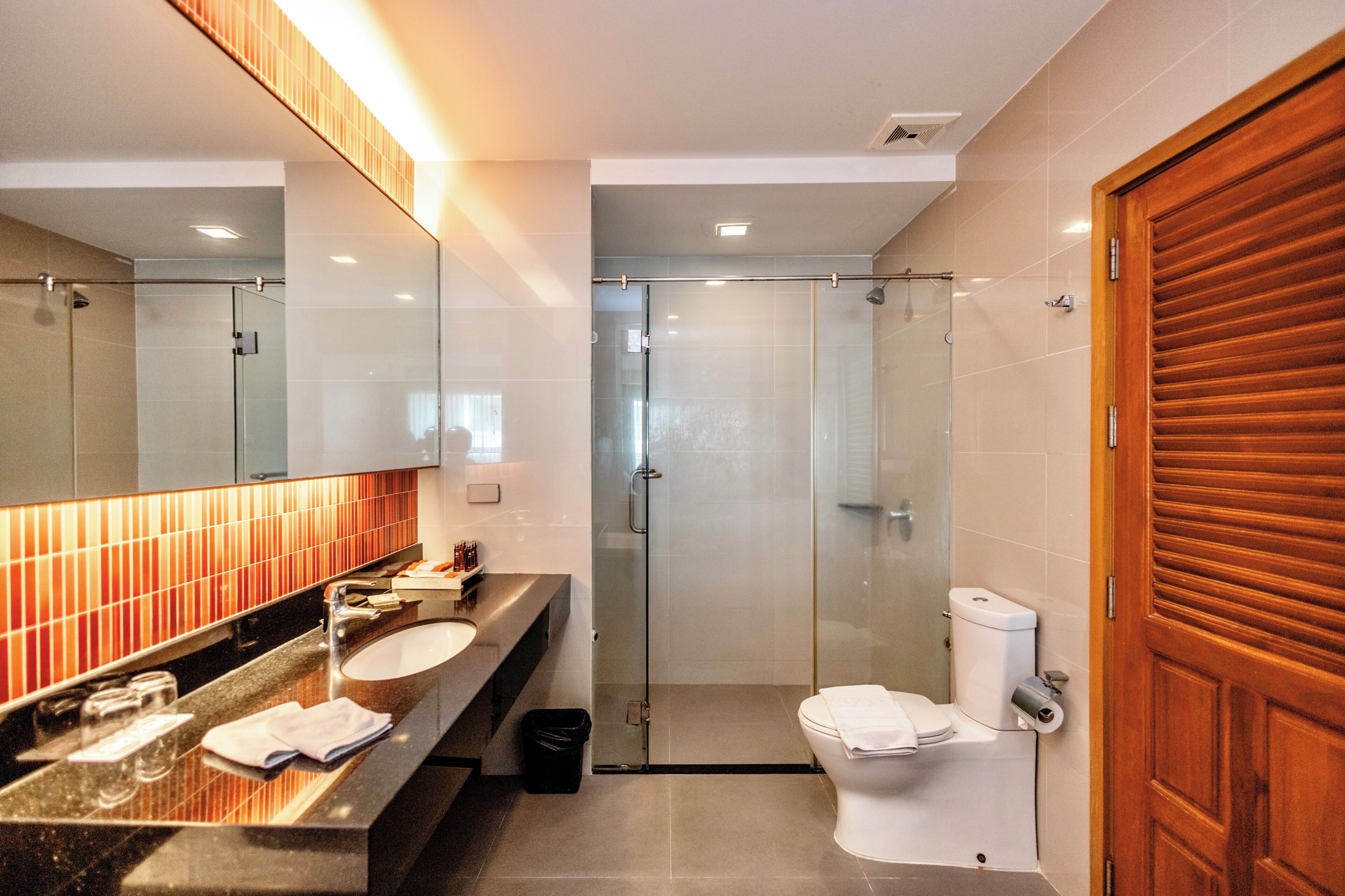 Un baño moderno con ducha de vidrio, inodoro blanco y tocador con espejo y lavamanos.