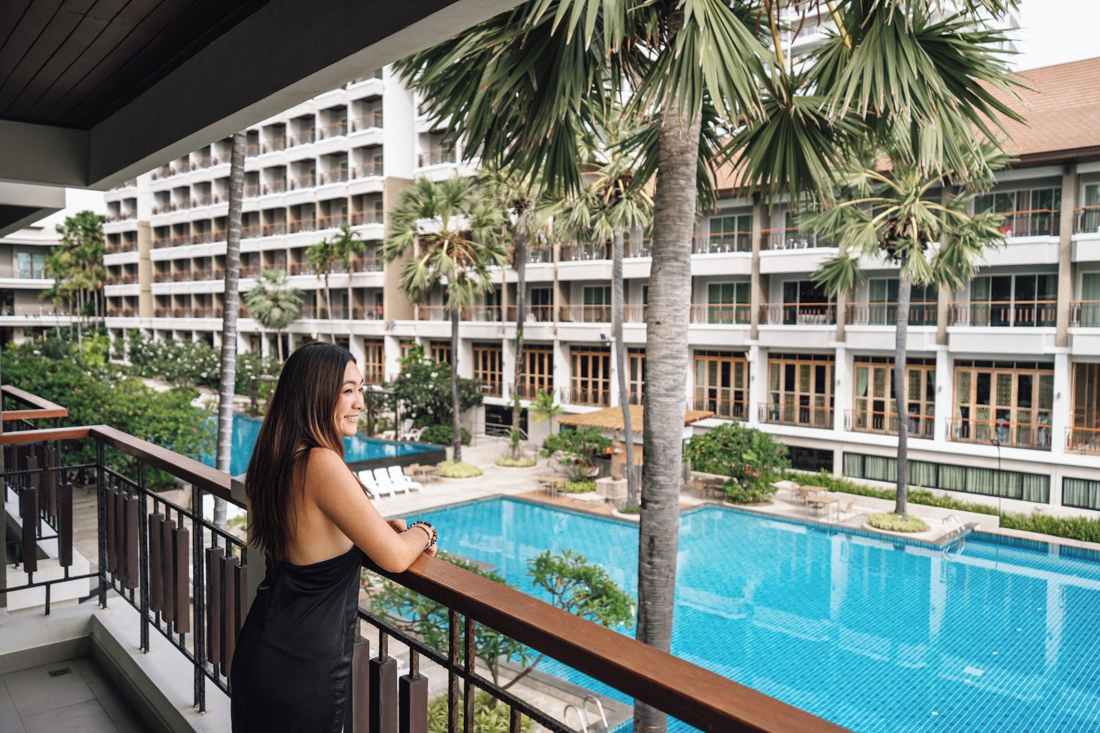 A hotel with a swimming pool, palm trees, and a balcony with a railing.
