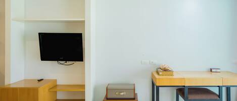 Une chambre moderne équipée d’un téléviseur à écran plat fixé au mur, d’un bureau en bois avec une chaise rembourrée et d’une petite table sur laquelle se trouvent une boîte et une télécommande.