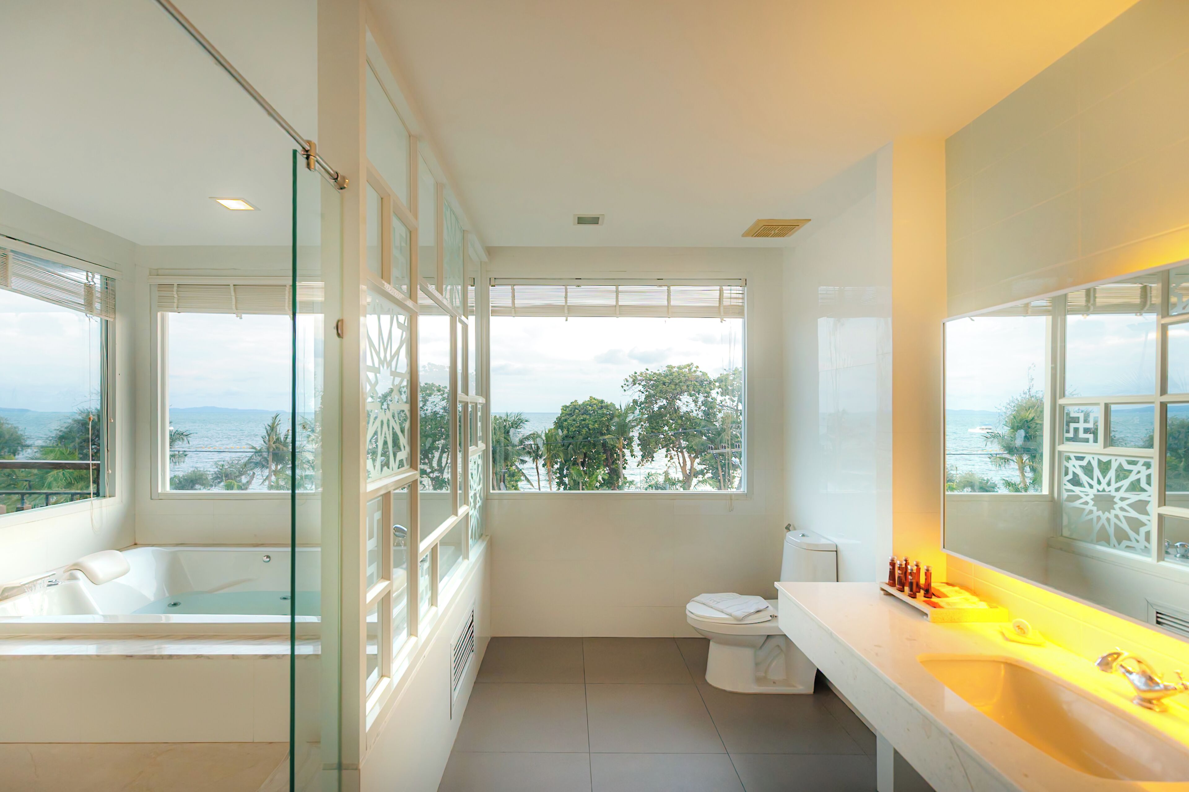 A modern bathroom with a bathtub, toilet, and large windows offering a view of the sea.