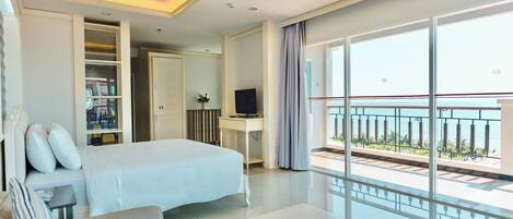 Quarto de hotel com cama, escrivaninha, televisão, varanda com grade e vista para o mar.