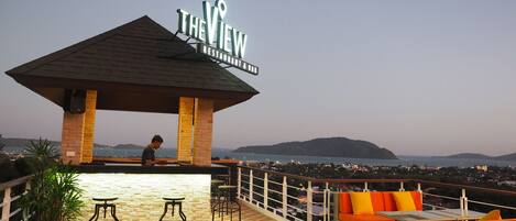 Une terrasse sur le toit avec un espace bar, des sièges extérieurs et une vue sur la ville et les collines.