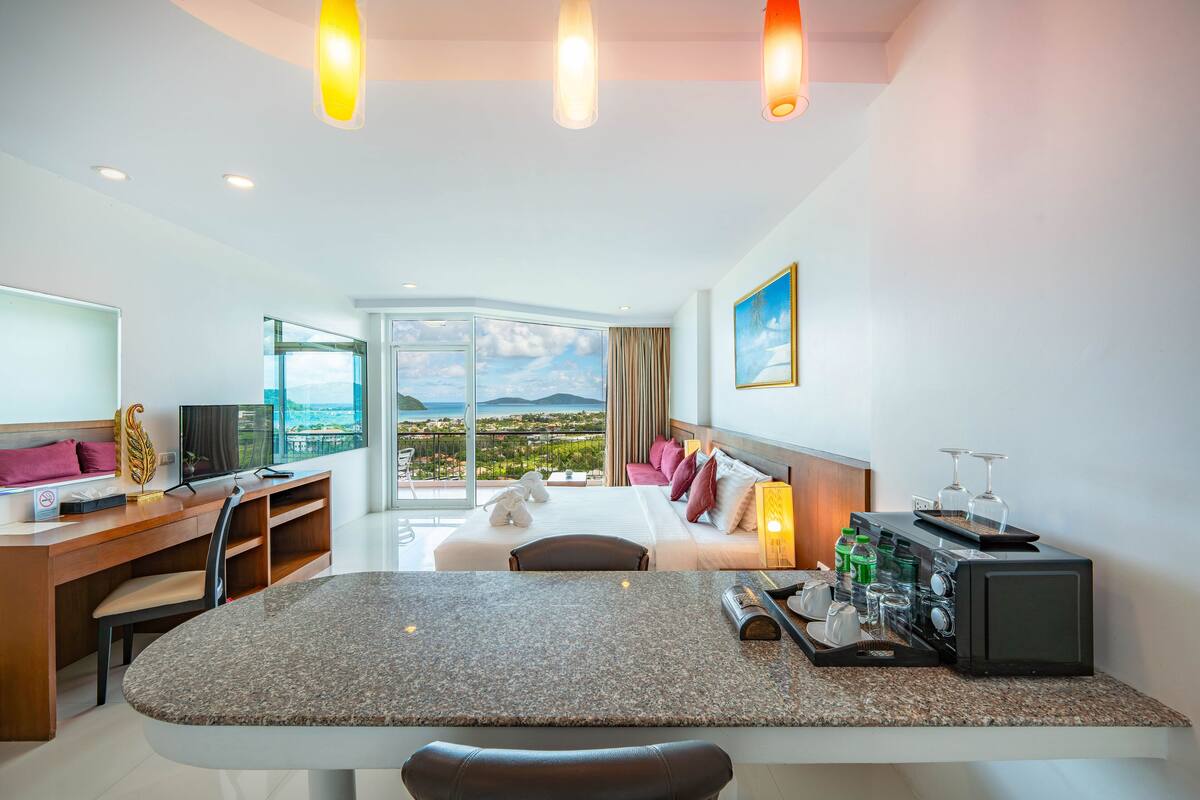 Une chambre d’hôtel moderne dotée d’un coin repas, d’un lit avec vue, d’un bureau avec ordinateur et d’une machine à café.