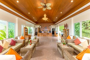 A spacious lobby with wicker furniture, a reception desk, and large windows offering a view of greenery.