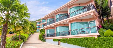 A multi-story hotel with balconies, lush greenery, and a clear sky.