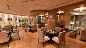 A spacious hotel lobby with multiple seating areas, including a dining area with tables and chairs, and a lounge area with sofas. - Boudl Al Maidan (Hafr Al Batin)