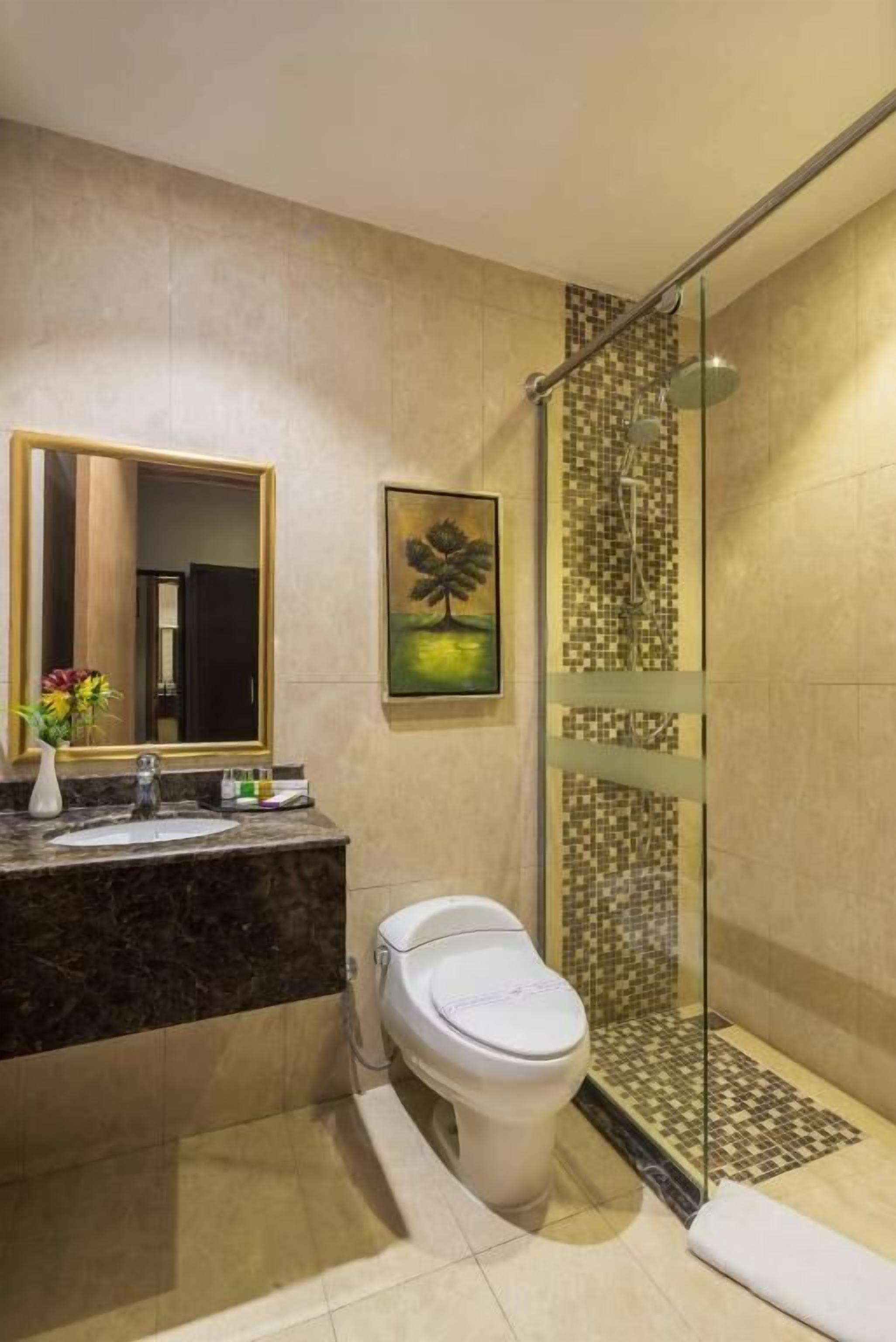 A modern bathroom with a marble sink, a toilet, a glass shower enclosure, and a large mirror.