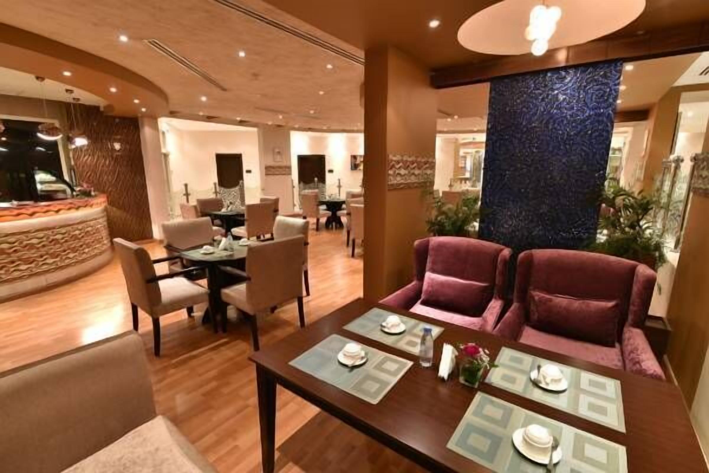 Un hall d’hôtel avec un espace repas comprenant une table en bois dressée pour deux personnes, entourée de fauteuils confortables.