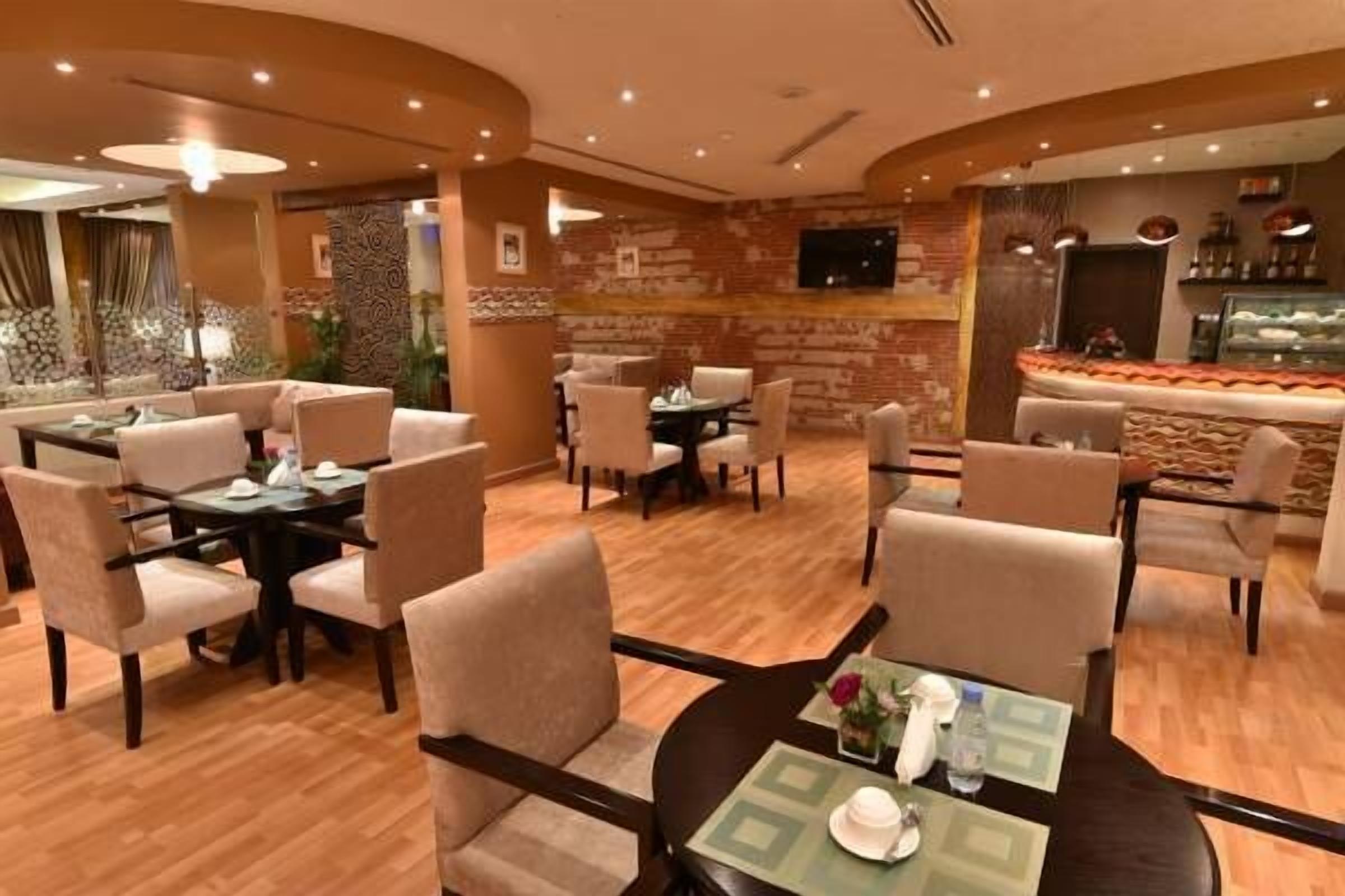 A restaurant with round tables and cushioned chairs, a brick wall, and a dessert display.