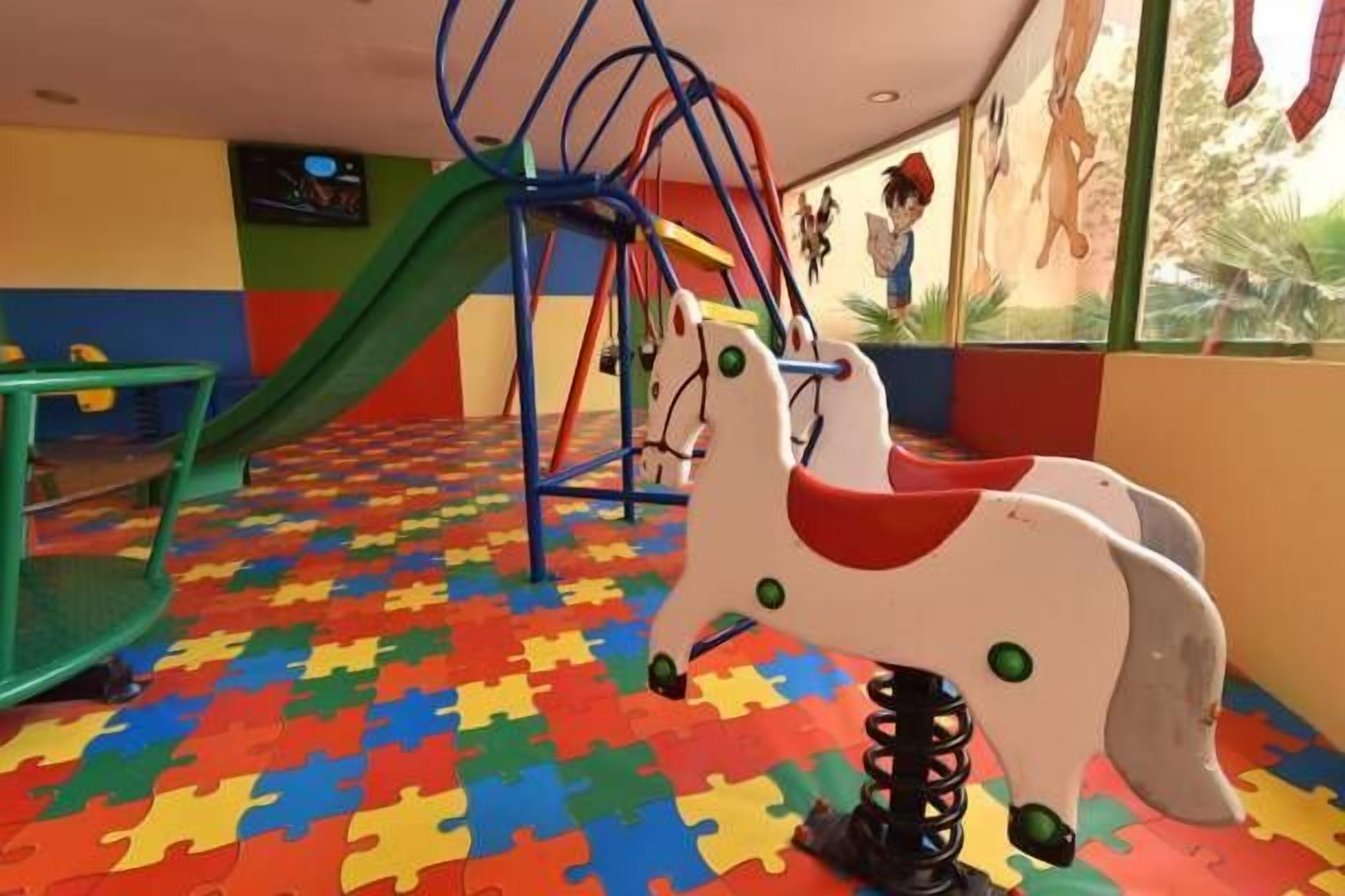 A play area with a colorful floor, a swing set, and a horse-shaped swing.