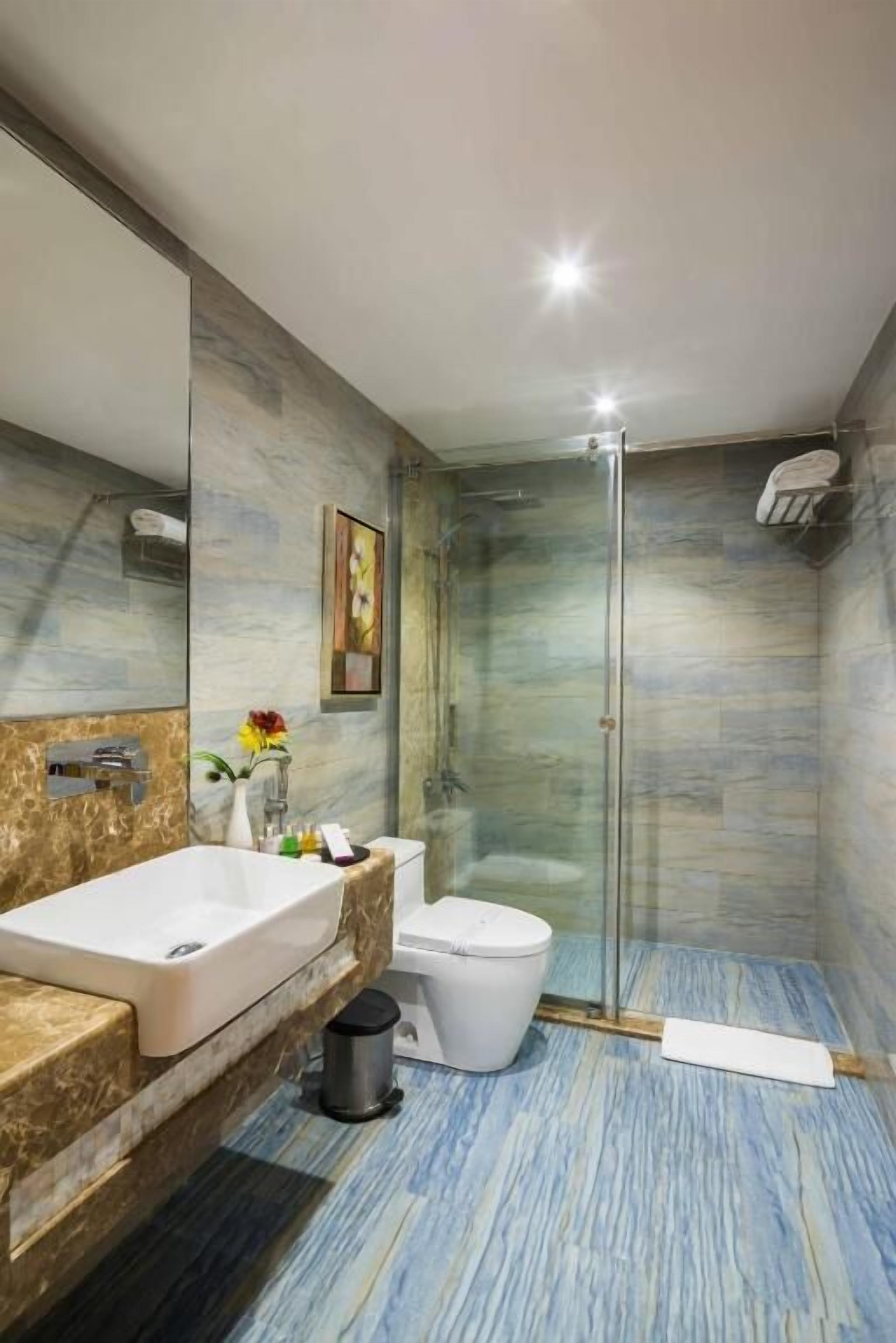 A modern bathroom with a marble vanity, a glass shower enclosure, and a toilet.